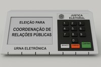 Imagem de urna eletrônica gerada por IA, com texto na tela: "Eleição para Coordenação de Relações Públicas"